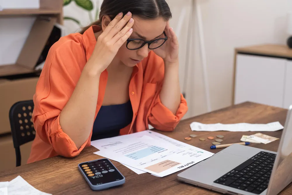Mulher preocupada com dívida de IPTU, analisando contas e calculadora.